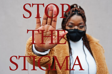 black woman with braided hair wearing white cardican, light brown jucket and black face mask. her right hand is raised, open palm facing forward. The words "Stop the Stigma" are written on the left side of the picture.
